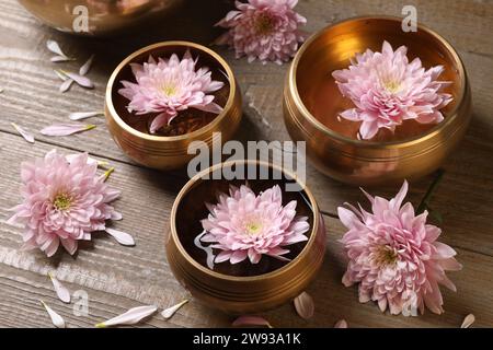Ciotole tibetane con acqua e bellissimi fiori su un tavolo di legno Foto Stock