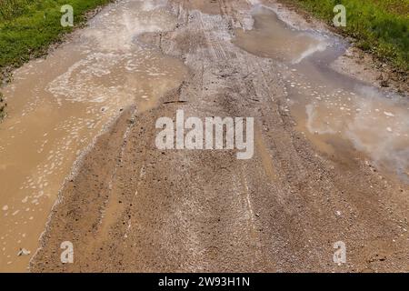 una strada di campagna coperta da pozze di acqua sporca, una strada sabbiosa in un campo dopo la pioggia Foto Stock