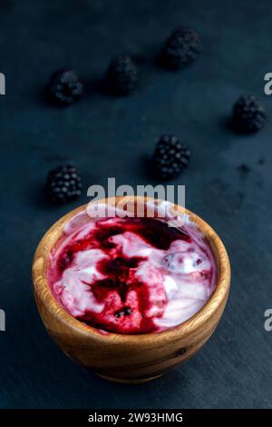 yogurt fresco con bacche di more succose tritate, preparazione di dessert allo yogurt con succo di frutta e bacche di more mature Foto Stock