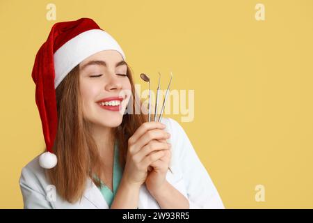 Giovane dentista di Babbo Natale con attrezzi dentali su sfondo giallo Foto Stock