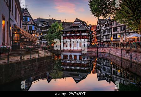 Case tradizionali in legno con fiori fioriti lungo i canali nel quartiere Petite France di Strasburgo, Alsazia, Francia al tramonto Foto Stock