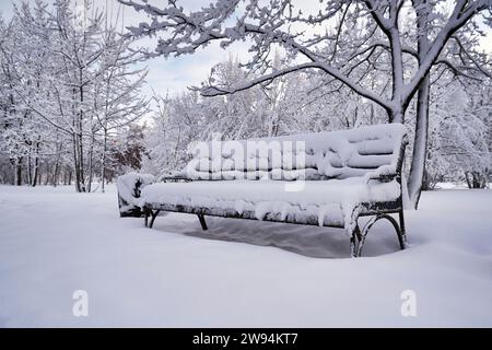 Una panchina in un parco cittadino coperto di neve Foto Stock