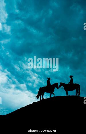 silhouette di due cowboy a cavallo in cima a una collina Foto Stock