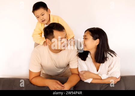 Felice famiglia asiatica a casa. Una coppia coreana e il loro bambino adorabile sul divano del soggiorno. I genitori e il loro figlio posano insieme. Foto Stock