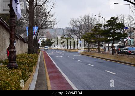 Una strada a due corsie con pista ciclabile separata dal traffico in entrata nel mezzo da una linea di alberi bonsai imperiali, intorno al palazzo Gyeongbokgung Foto Stock