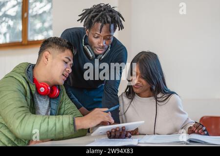 Tre studenti multiculturali partecipano a una sessione di apprendimento interattiva con appunti e dispositivi digitali, condividendo le conoscenze. Foto Stock