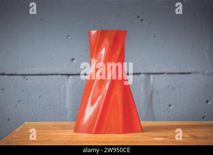 Vaso oggetto rosso brillante stampato da stampante 3d su sfondo murale blu. La stampante 3d tridimensionale automatica esegue la modellazione dei colori rosso-plastica in laboratorio. Moderna tecnologia di stampa 3D. Foto Stock