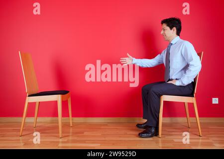 Accordo di stretta di mano tra un imprenditore e una sedia accanto ad una parete rossa Foto Stock