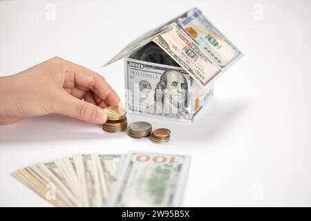 casa fatta di dollari, sfondo bianco, monete che salvano le mani Foto Stock