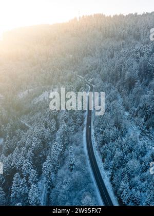 Una strada solitaria si snoda attraverso una fitta foresta innevata, Dobel, vista aerea, Foresta Nera, Germania Foto Stock