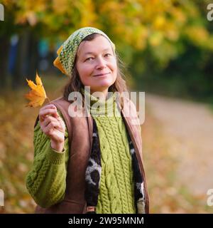 Ritratto di donna nel parco autunnale con foglia d'acero gialla. Ritratto di una donna di 52 anni Foto Stock