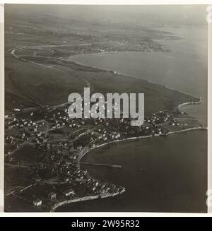 Foto aerea in bianco e nero di una città o villaggio, situata sull'acqua, con prati sullo sfondo, situata su una baia con una banchina, Anonimo, 1930 - 1975 Fotografia aerea in bianco e nero di una città o villaggio, situata sull'acqua, con prati sullo sfondo, situati su una baia con una banchina (fronte). supporto fotografico stampa in argento gelatina Foto Stock