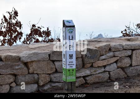 Un marcatore di altitudine sulla cima del monte Nahabong di fronte a un muro di pietra nel Parco Nazionale di Bukhansan Foto Stock