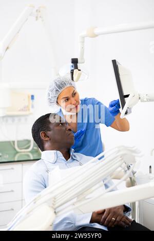 Dentista donna che indica il display per mostrare le informazioni al paziente Foto Stock