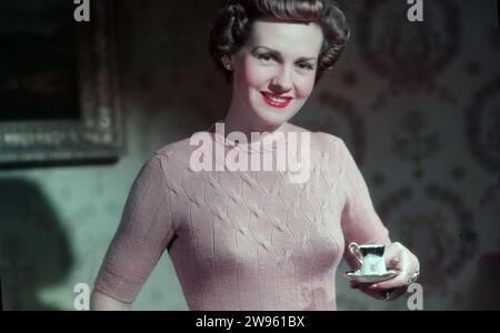 Anni '1950, storico, rosa inglese, moda femminile dell'epoca, una giovane donna che indossa una vestibilità aderente, girocollo, top in lana rosa chiaro, con una tazza di tè cinese con osso piccolo, Inghilterra, Regno Unito. Tessuti morbidi e delicati come la lana hanno giocato un ruolo importante nella moda femminile negli anni '1950 Foto Stock