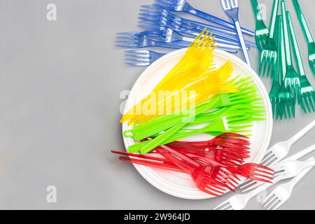 Stoviglie in plastica colorata e luminosa. Forche in plastica, cannucce sulla piastra. Bicchieri colorati di carta. Riutilizzo, concetto ambientale. Spianatura piatta. Sfondo grigio Foto Stock