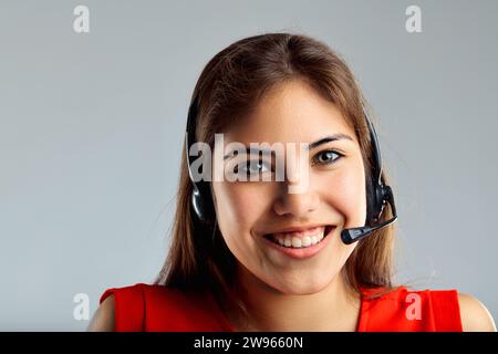 L'operatore di supporto entusiasta sorride calorosamente e la sua cuffia suggerisce una conversazione in corso Foto Stock