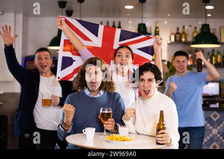 Compagnia di gioiosi tifosi sportivi sventolando la bandiera della Gran Bretagna e celebrando la vittoria della squadra favotite in pub Foto Stock