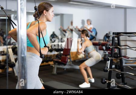 Giovane trainer nella sala della palestra, il centro fitness lavora con i muscoli di braccia e spalle sull'apparato di allenamento, macchina per esercizi Cable Crossover. Ragazza Foto Stock