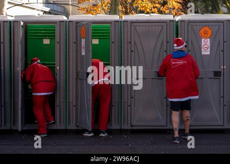 Le persone vestite da Babbo Natale aspettano di utilizzare i bagni pubblici dopo aver corso durante la tradizionale corsa annuale di Natale di Babbo Natale. Una gara annuale di beneficenza che quest'anno aiuterà la Croce Rossa spagnola. Foto Stock