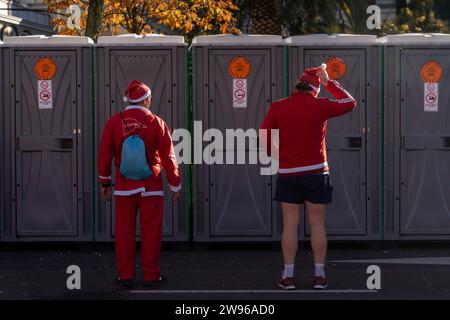 Le persone vestite da Babbo Natale aspettano di utilizzare i bagni pubblici dopo aver corso durante la tradizionale corsa annuale di Natale di Babbo Natale. Una gara annuale di beneficenza che quest'anno aiuterà la Croce Rossa spagnola. Foto Stock