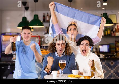 Tifosi felici con la bandiera dell'Argentina, gioendo gioco vincente con birra e spuntini in pub Foto Stock