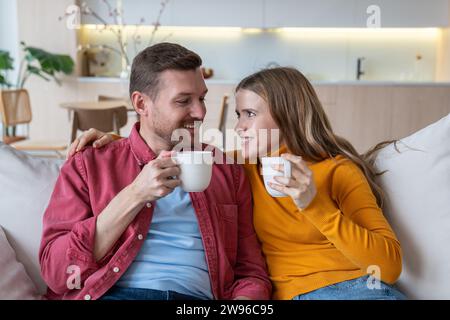 Adorabile coppia sposata che passa passatempo, weekend a casa, sedersi sul divano, chiacchierare, bere un tè Foto Stock