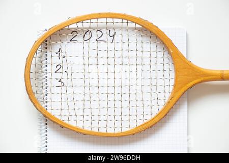 Una racchetta da badminton si trova su un blocco note e il testo 2024 e 123 è scritto in un blocco note su sfondo bianco, sport nel nuovo anno 2024 Foto Stock