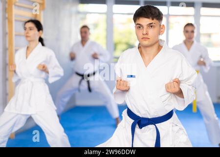 Gruppo di uomini e donne in kimono addestrano tecniche di karate in studio. Foto Stock