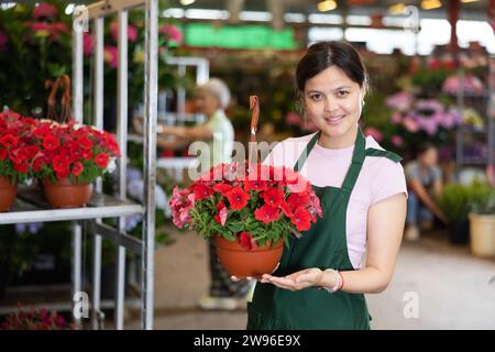 Allegra venditrice asiatica di negozi di fiori che organizzano petunias in fiore in vasi appesi su bancarelle di fiori. Foto Stock