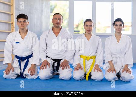 Gruppo di uomini e donne karateka in kimono in posa mentre sedevano sul pavimento in studio. Foto Stock