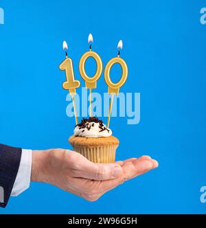 Dolce di compleanno consegnato a mano - candela numero 100 su sfondo blu Foto Stock