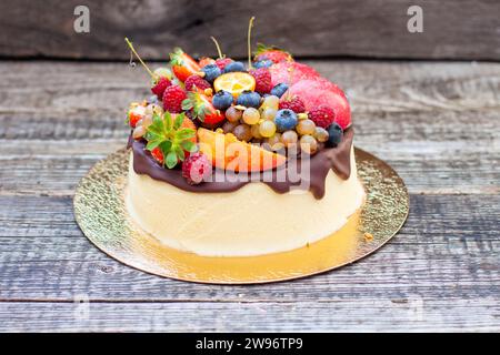 Deliziosa cheesecake con cioccolato fuso, mele, fragole, mirtilli, pesche, lamponi e kumquat in cima, sfondo rustico Foto Stock