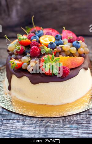 Deliziosa cheesecake con cioccolato fuso, mele, fragole, mirtilli, pesche, lamponi e kumquat in cima, sfondo rustico Foto Stock