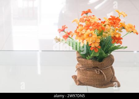 bellissimi e colorati fiori artificiali fatti di stoffa sono confezionati in una piccola borsa marrone su un tavolo di vetro trasparente preso dallo showroom dell'auto. Foto Stock