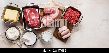 Grassi saturi sui tavoli. Carne cruda, salsicce, formaggio, burro. Cattivo concetto di cibo. Vista dall'alto, banner, spazio di copia. Foto Stock