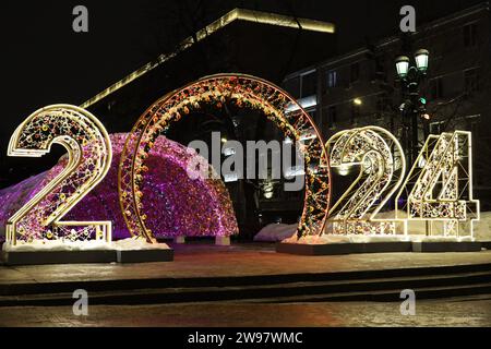 Decorazioni di Capodanno in una strada notturna della città con grandi numeri 2024. Illuminazione festiva, festeggiamenti di Natale Foto Stock