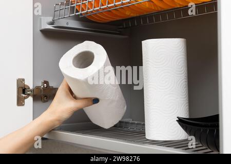 la mano di una donna tira fuori un tovagliolo di carta dall'armadio. la casalinga prende un rotolo di carta assorbente dall'armadio della cucina Foto Stock
