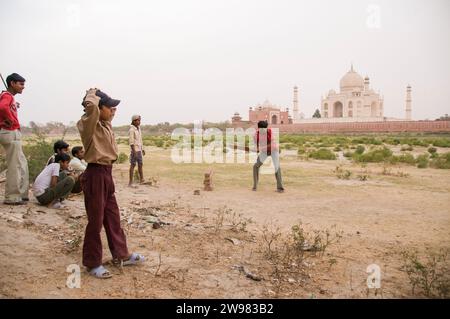 Un gruppo di giovani uomini e ragazzi giocare un pick-up gioco di cricket, con il Taj Mahal in background, Agra, India. Foto Stock