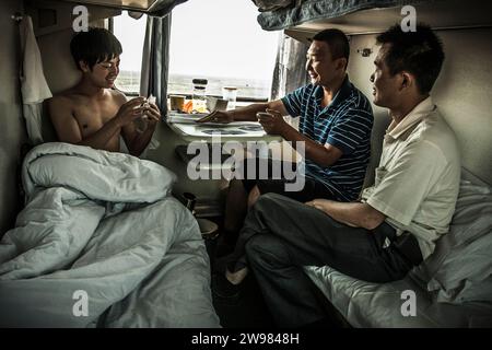 I passeggeri giocano a carte dai loro letti mentre sono su un treno in Cina. Foto Stock