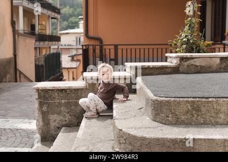 Una bambina siede sui gradini di una casa in una tipica città italiana Foto Stock