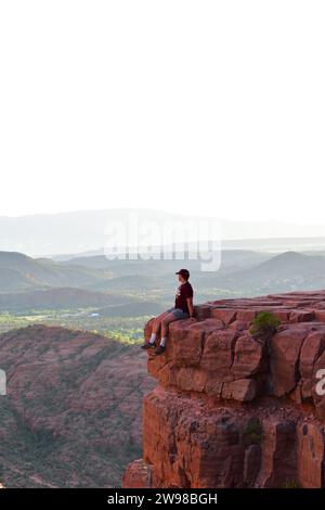 Persona seduta su una sporgenza di pietra che si affaccia sul paesaggio desertico dell'Arizona dalla Cathedral Rock di Sedona Foto Stock