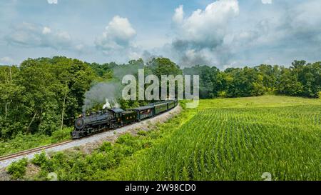 Una vista aerea di un treno passeggeri a vapore a scartamento ridotto, avvicinandosi attraverso la campagna, soffiando fumo, in una soleggiata giornata estiva Foto Stock