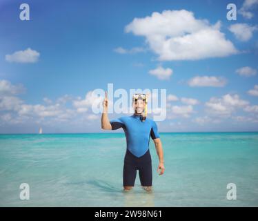 Giovane uomo che indossa un costume da immersione e una maschera e punta in alto nel mare Foto Stock