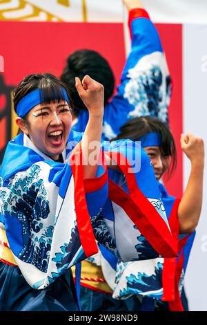 Primo piano, giovane ballerino giapponese yosakoi che danza con il braccio sollevato con un pugno stretto mentre applaude. Indossa la tunica yukata blu e bianca. Foto Stock