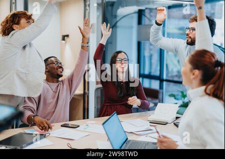 I colleghi multietnici celebrano un successo. Sorridendo e alzando le armi, mostrano lavoro di squadra, risultati e vittoria in ufficio. Foto Stock