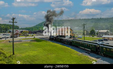 Una vista aerea di un treno passeggeri a vapore a scartamento ridotto, arrivando alla stazione, soffiando fumo, in una soleggiata giornata estiva Foto Stock