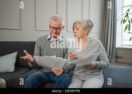 Triste stanco, deluso, coppia di anziani di mezza età siedono con un documento cartaceo. Infelice anziano maturo donna che legge banconote che gestiscono le finanze bancarie calcolano le tasse pianificazione prestito pagamento pensione Foto Stock