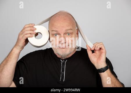 Uomo di mezza età con rotolo di carta igienica come sopra o sotto concetto su sfondo grigio Foto Stock