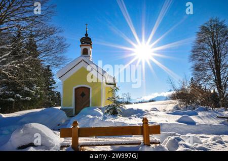 Ripresa in controluce della Maria Chapel, ricoperta di neve, sulla Buckelwiesen Werdenfelser Land vicino a Garmisch in un idillio del vento, con le montagne Karwendel Foto Stock